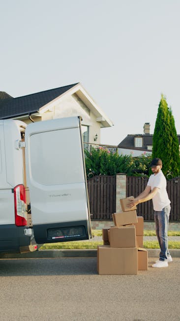 Inside the rear of a white van belonging to Man With a Van Hornchurch, several stacked cardboard boxes are visible, neatly arranged for home relocation. Two individuals are actively involved in the fu